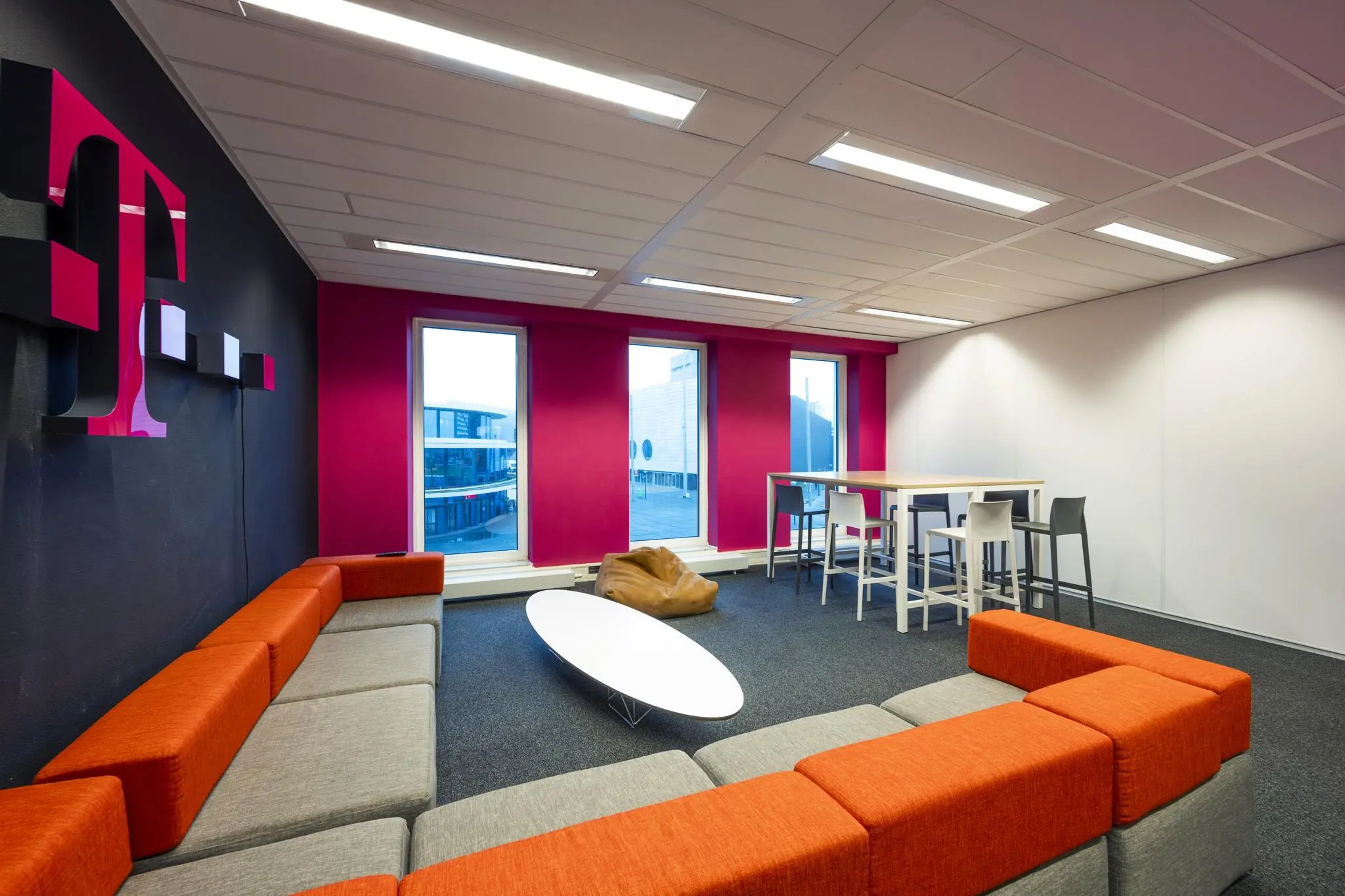 Moderne lounge- en werkruimte met kleurrijke zitbanken, een grote T-Mobile wandlogo en uitzicht op de Johan Cruijff Boulevard.